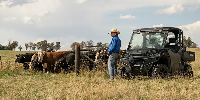 A Can-Am Defender loaded with gear on a Texas ranch with cattle in the background.