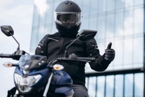 Motorcycle rider wearing a full-face helmet and protective jacket, giving a thumbs up for safe riding practices.