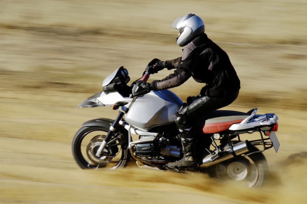 A motorcyclist in full safety gear riding a silver adventure bike through a dusty field, highlighting competitive motorcycle financing options.